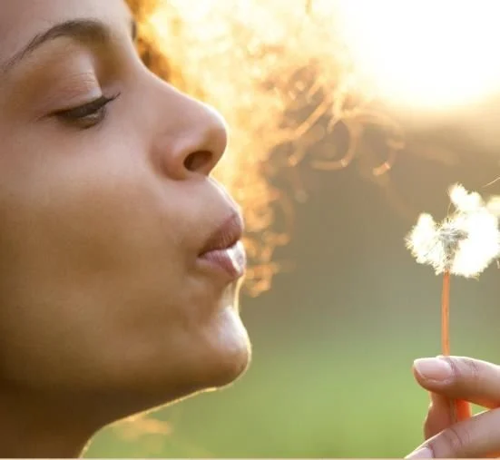 A young woman blowing a dandelion in the sunlight