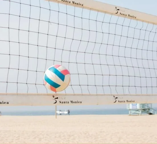 A volleyball above the net on a beach court